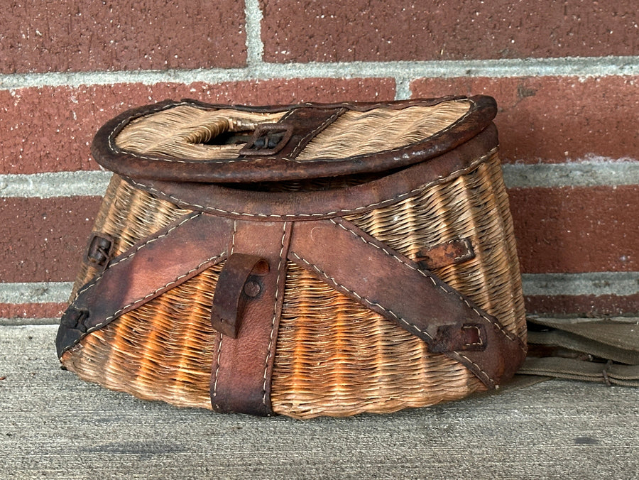 Woven fishing basket with leather straps against a brick wall